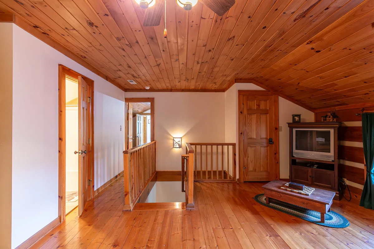 A cozy lounge space with a wooden ceiling and railing, a television, and a central coffee table. This area is designed for relaxing, watching TV, or enjoying board games together, with an inviting ambiance and plenty of seating for groups.