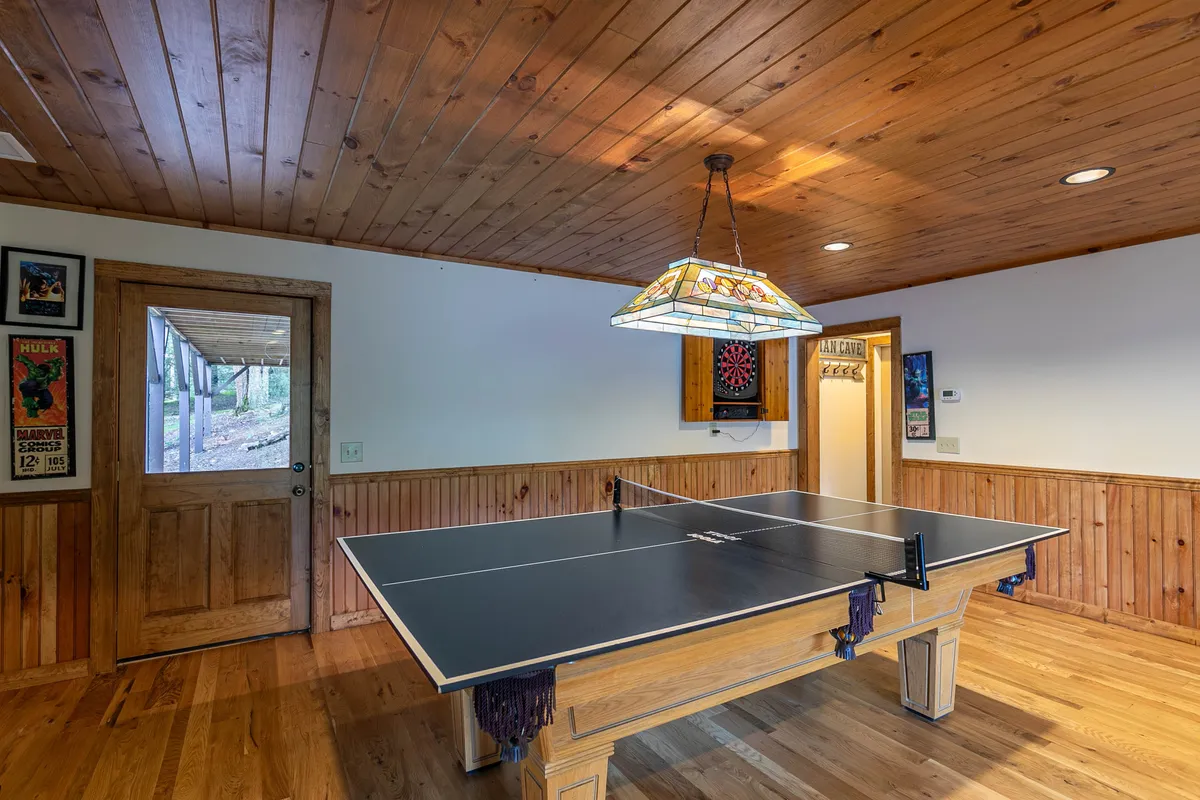 This image features a vibrant entertainment area centered around a ping pong table, with a distinctive stained glass lamp hanging above and a dart board on the wall. The atmosphere is playful and relaxed, with wooden doors and cozy details suggesting a dedicated space for games and friendly competition.