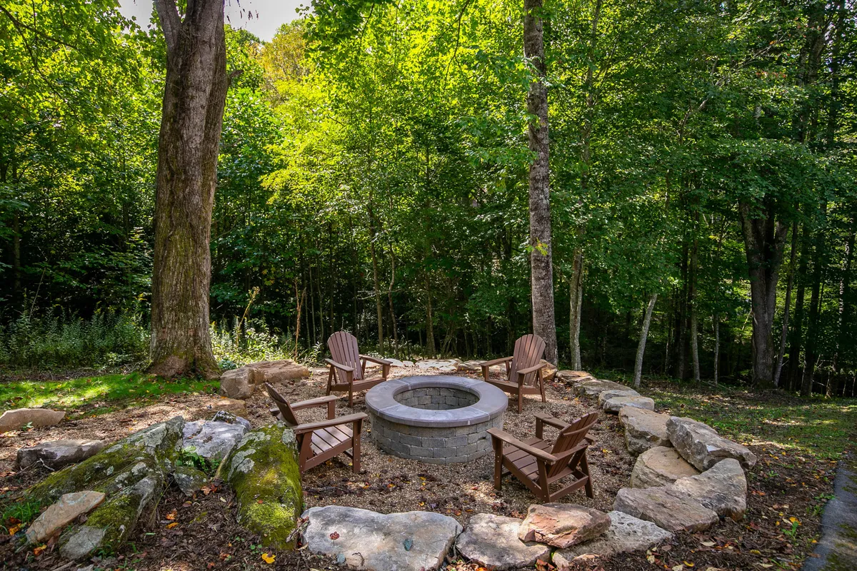 An inviting fire pit area surrounded by Adirondack chairs, natural rock formations, and trees, creating a cozy atmosphere for evening gatherings. The setting is perfect for storytelling, laughter, and stargazing under the open sky.