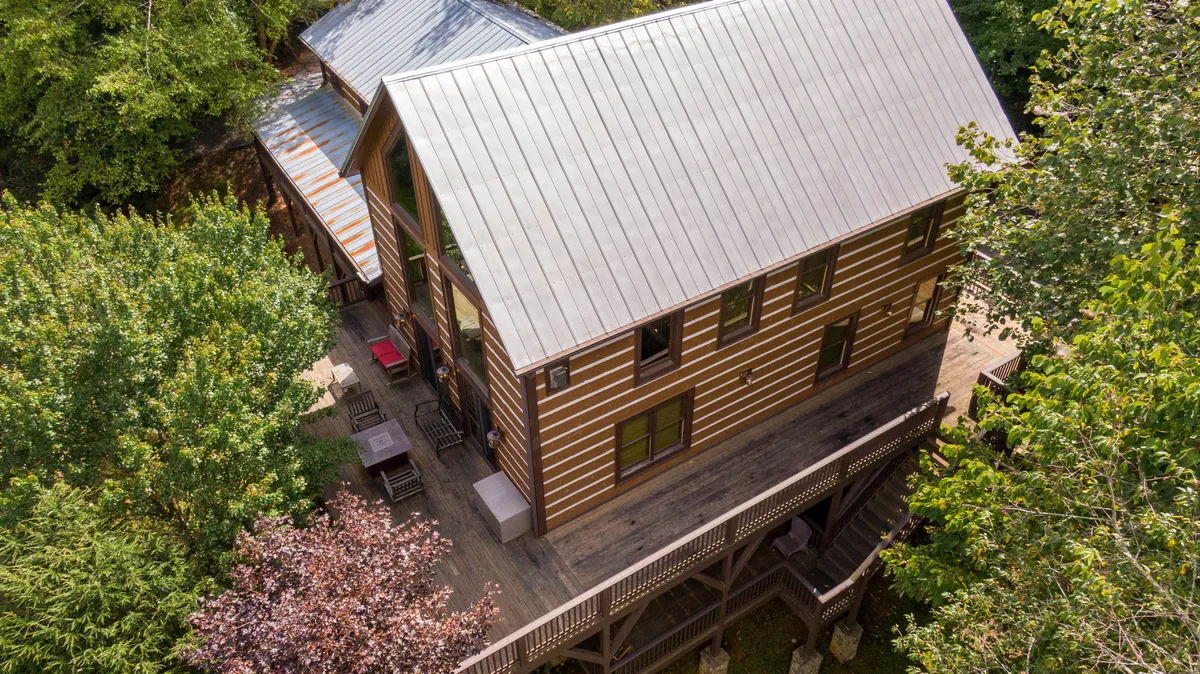 A charming log cabin with a metal roof sits surrounded by trees, featuring an inviting deck area. The outdoor space is ideal for dining, stargazing, or soaking up the serene natural environment. The scene evokes a sense of escape and privacy, integral to the relaxation theme.