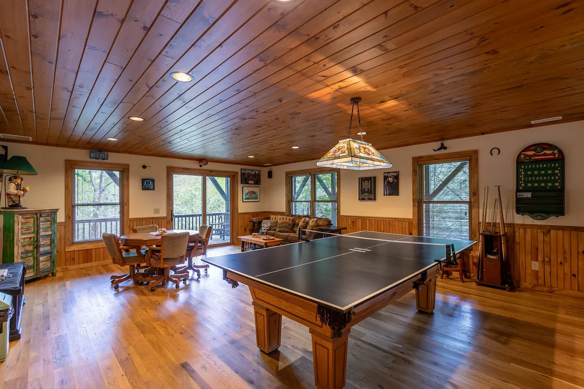 A welcoming game and lounge area featuring a ping pong table at the center, comfortable sofa seating, a dining table for board games or snacks, and large windows providing natural light. The layout is open, making it easy for groups to mingle and enjoy different games or relax at once.