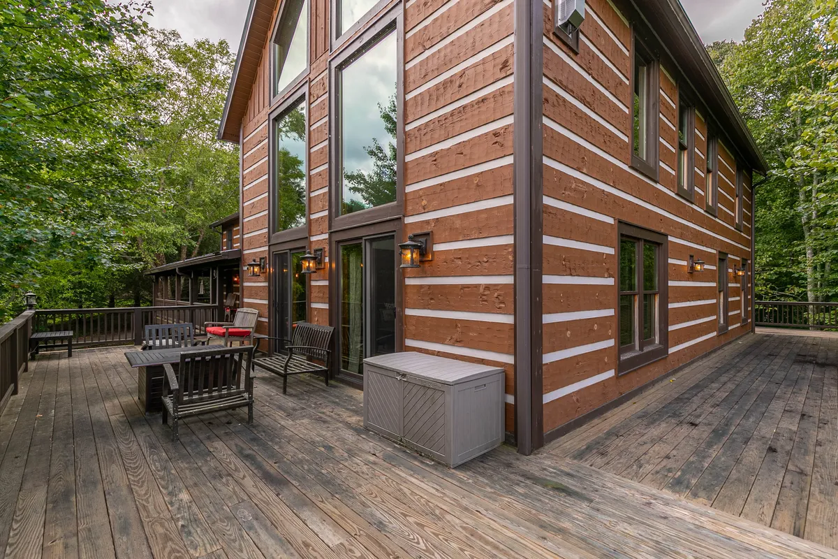 Showcasing a wooden deck with comfortable outdoor seating, lanterns for nighttime ambiance, and expansive windows connecting inside and outside. The area invites guests to socialize, dine al fresco, or unwind after a day of adventure, all with a scenic natural backdrop.