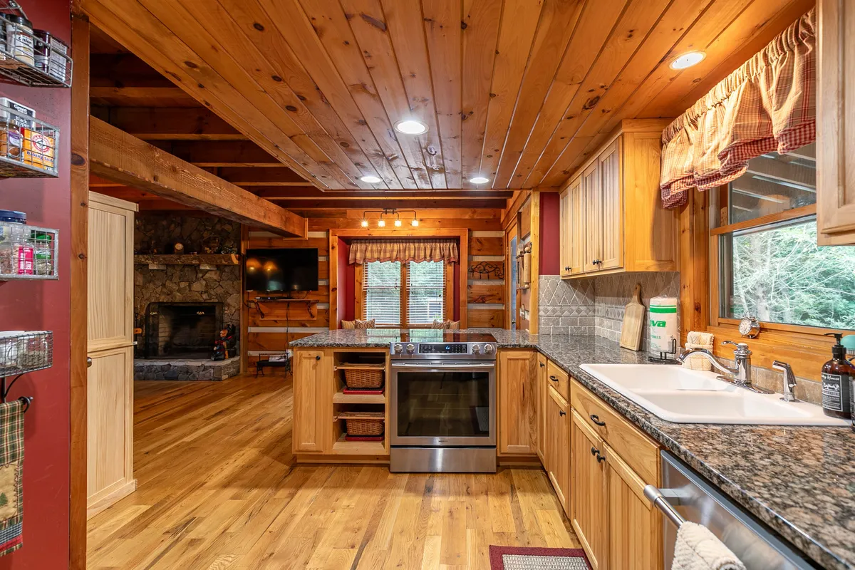 A spacious kitchen area with a prominent kitchen island, granite countertop, wooden cabinetry, a fireplace near the dining area, and a large window bringing in natural light. The layout encourages group gatherings and easy meal preparation.